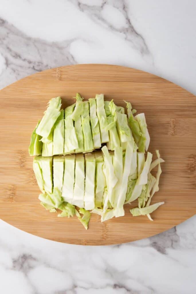 Cut up green cabbage on wooden cutting board.