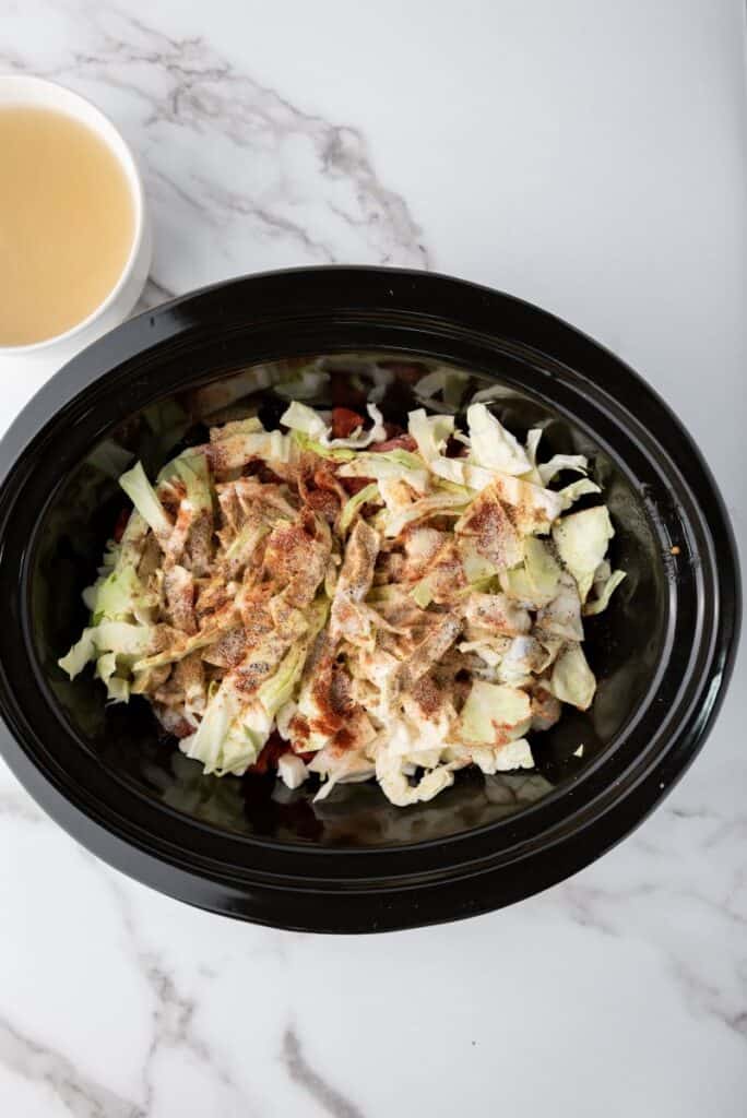 Cabbage topped with seasonings in black slow cooker.