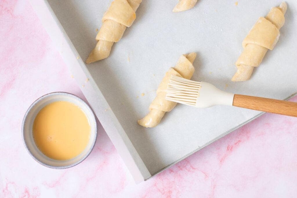 Top view of brushing beaten egg on unbaked croissants.