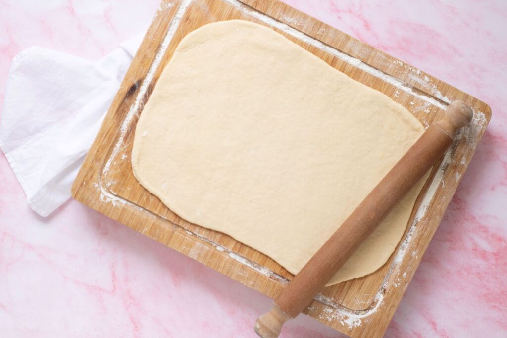 Flattened croissant dough on wooden cutting board.