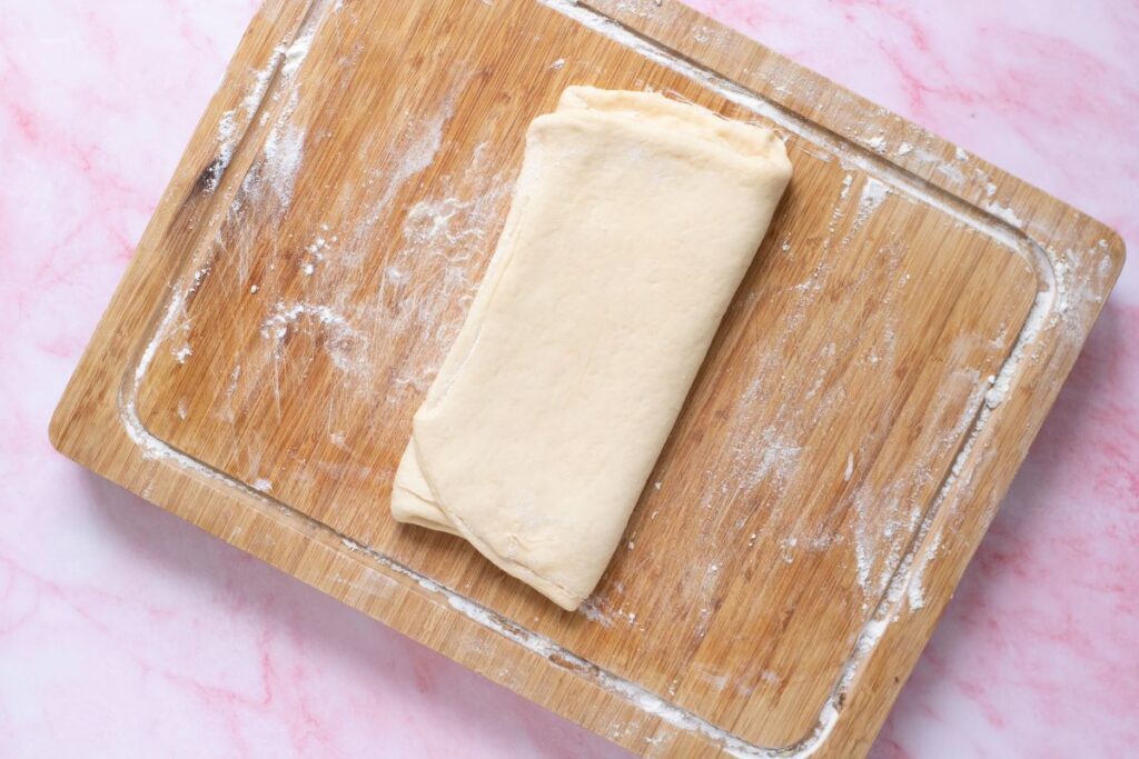 Folded croissant dough on wooden cutting board.