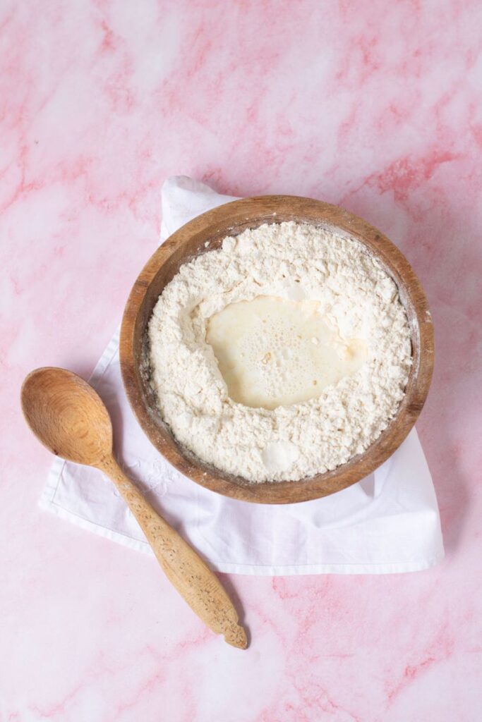 Flour and milk in wooden bowl next to wooden spoon.