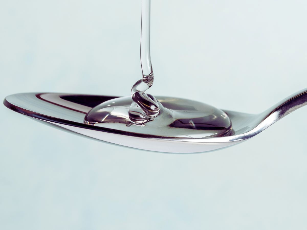 Thick clear liquid flowing onto silver spoon from above.
