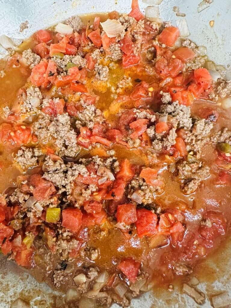 Cooked hamburger, tomatoes, green chilies, and onions in aluminum skillet.