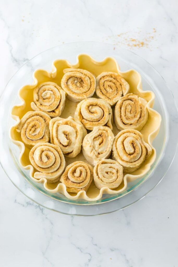 Top view of uncooked cinnamon rolls in uncooked pie crust.