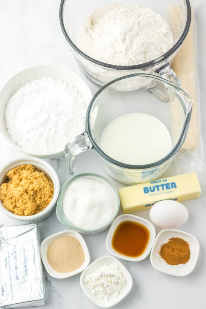 Ingredients for cinnamon roll pie in glass bowls on white surface.