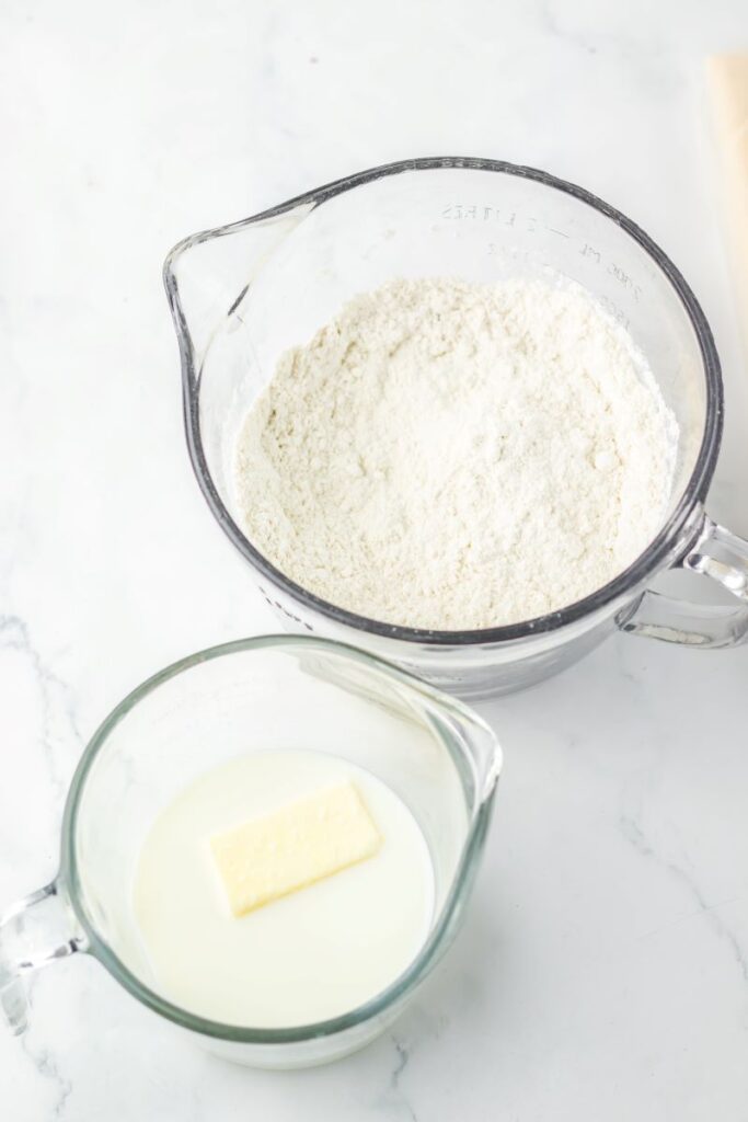 Two glass measuring cups, one with flour and one with milk and a stick of butter.