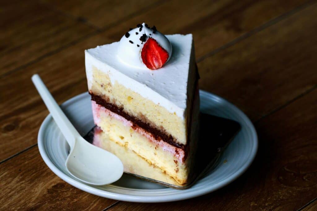 Slice of white cake with pink filling and white frosting on white plate.