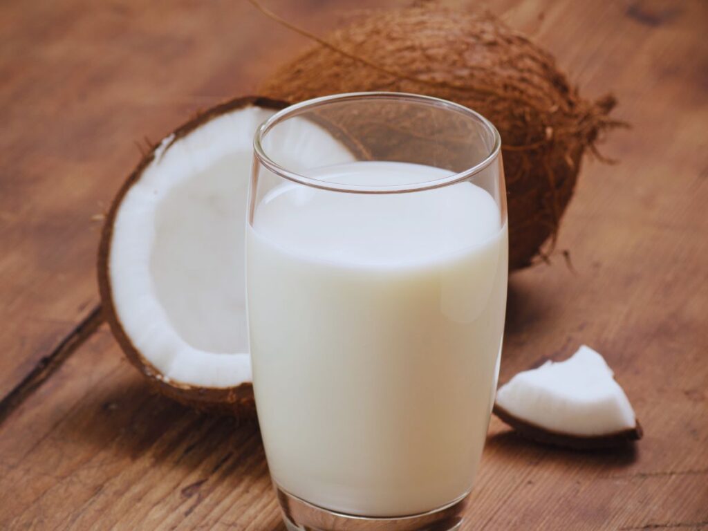 Close up of clear glass of milk with open coconut in the background.