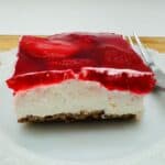 Side view of a slice of strawberry pretzel salad with three layers - pretzel crust, white creamy middle, and red jello and strawberry top.