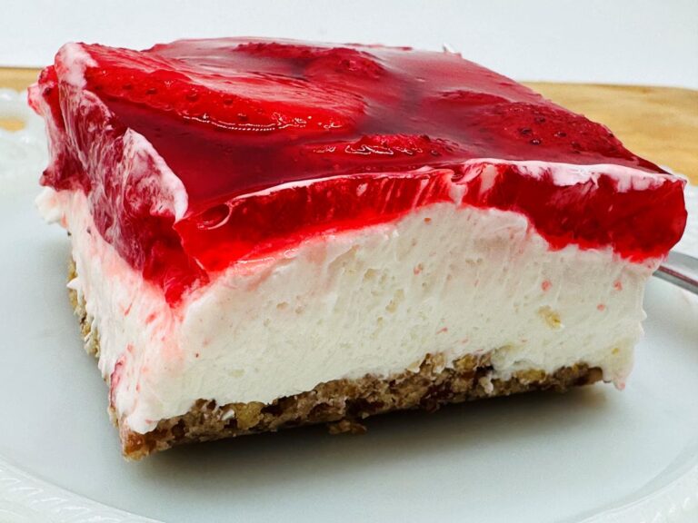 Side view of a slice of strawberry pretzel salad with three layers - pretzel crust, white creamy middle, and red jello and strawberry top.