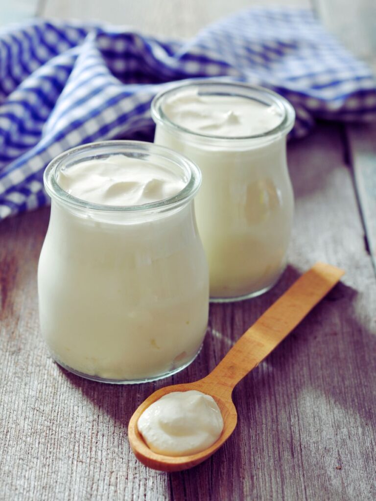 Two clear jars of white yogurt with wooden spoon in front.