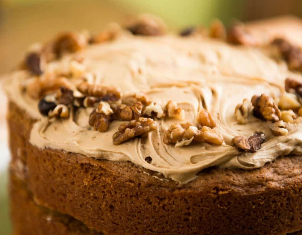 Close up of light brown cake with light brown frosting and walnuts on top.