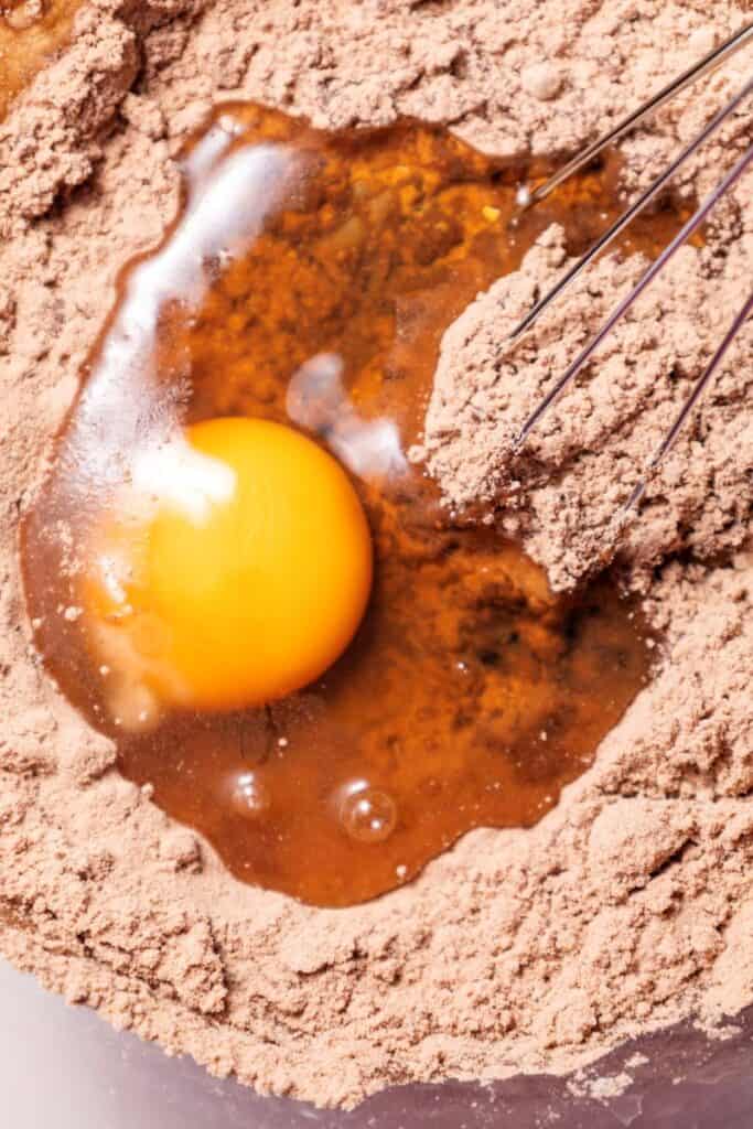 Egg white and yolk in brown powder with whisk.