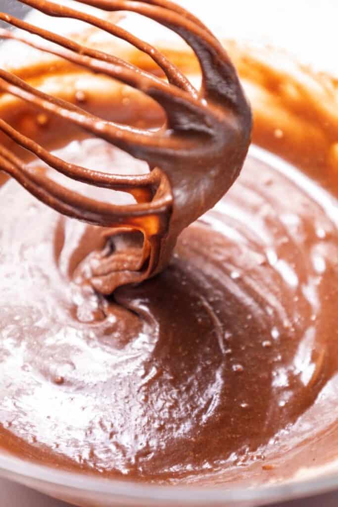 Whisk with brown batter above bowl of brown batter.