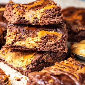 Stack of chocolate peanut butter brownies next to more brownies and a spoonful of peanut butter.