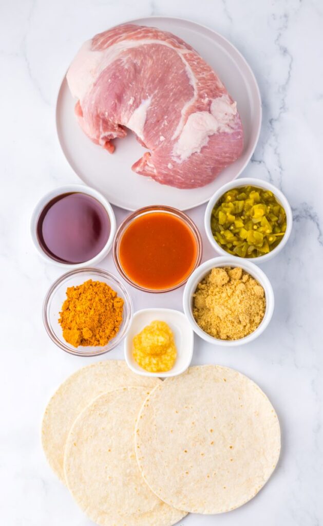 Top view of ingredients for slow cooker shredded pork tacos in clear bowls on white marbled surface.