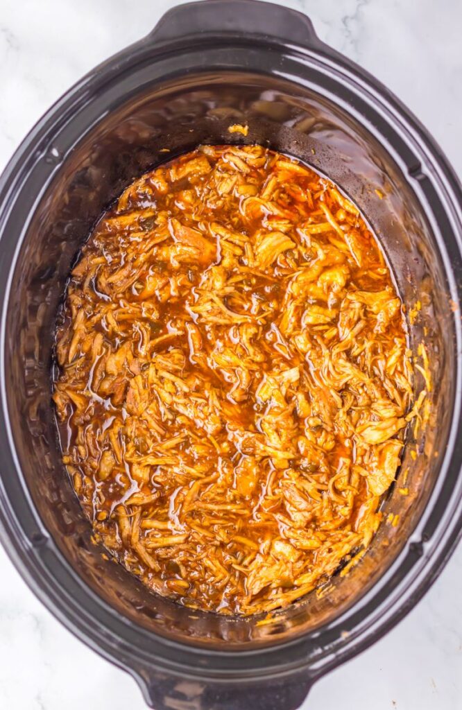Top view of shredded pork in dark brown liquid in slow cooker.
