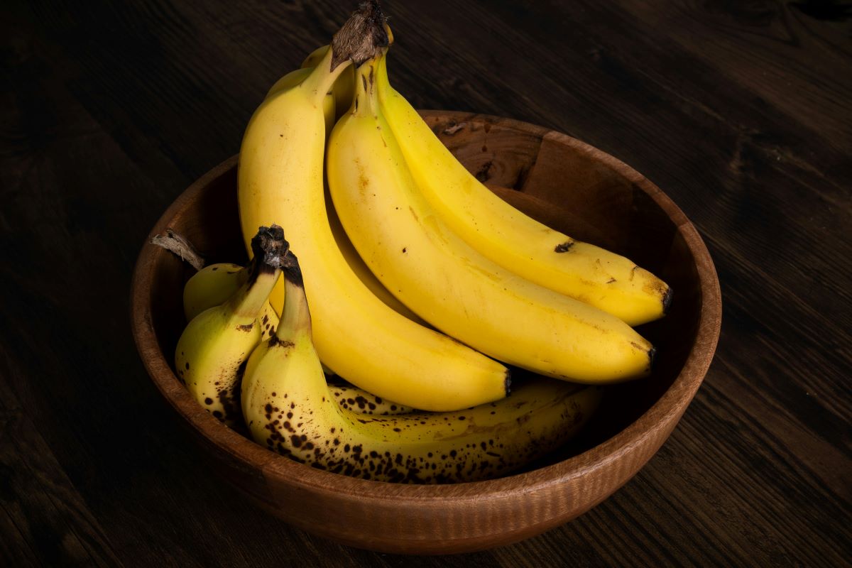 Two bunches of bananas in wooden bowl on wooden background.