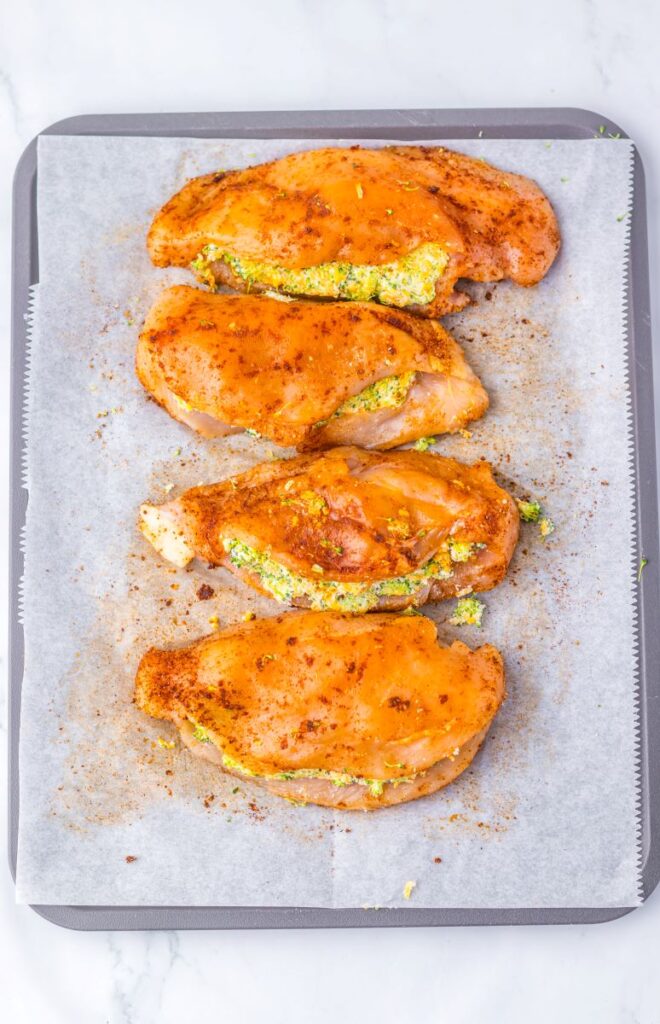 Raw chicken stuffed with broccoli and cheese on parchment paper.
