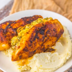 Close up of cooked chicken on white plate with mashed potatoes.