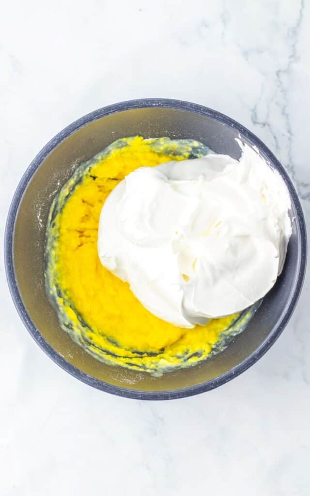 Top view of whipped topping added to yellow mixture in blue bowl.
