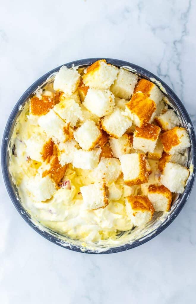 Cubed angel food cake on top of yellow mixture in blue bowl.