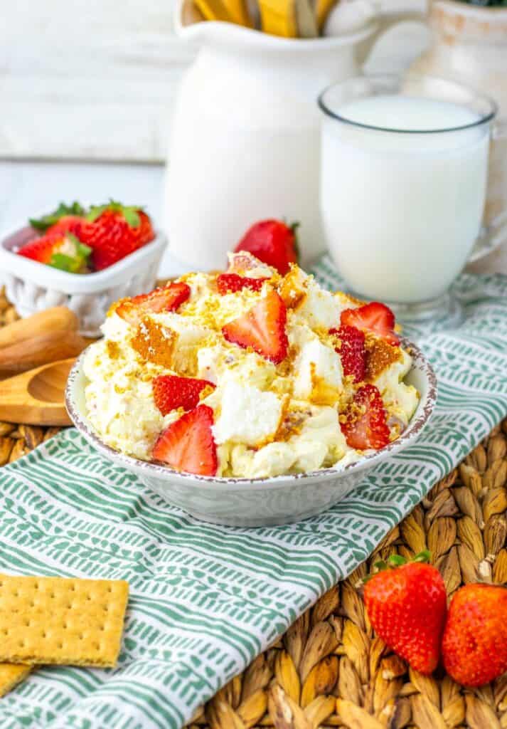 Angled view of strawberry shortcake fluff salad on green and white towel with milk and strawberries in the background.