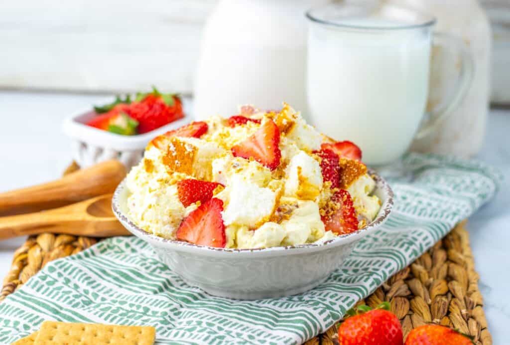 Angled view of strawberry shortcake fluff salad on green and white towel with milk and strawberries in the background.