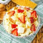 Top view of strawberry shortcake fluff salad in white bowl on green and white towel with graham crackers in the background.