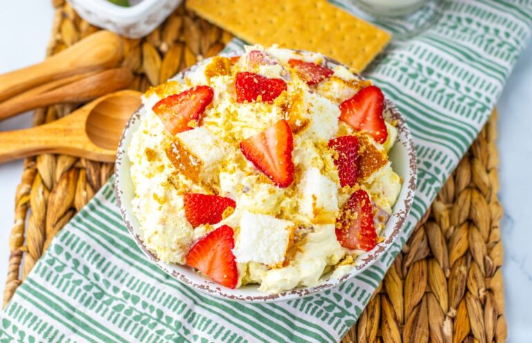 Top view of strawberry shortcake fluff salad in white bowl on green and white towel with graham crackers in the background.