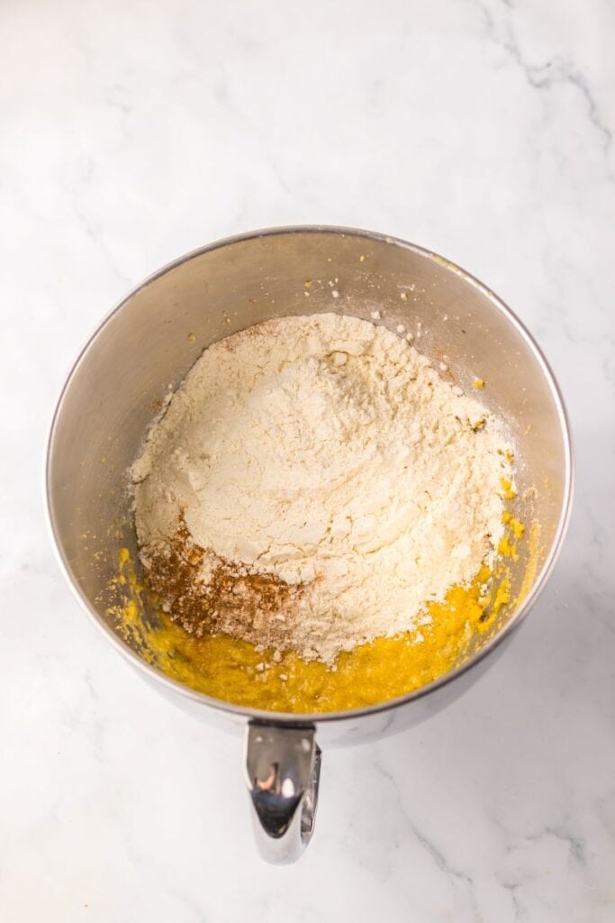 Silver bowl with baking soda, flour, cinnamon, vanilla, eggs, brown sugar, and butter.