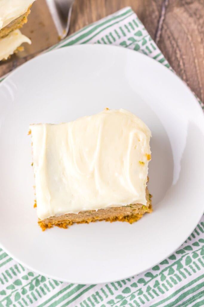 Top view of square slice of zucchini cake with white frosting on white plate.