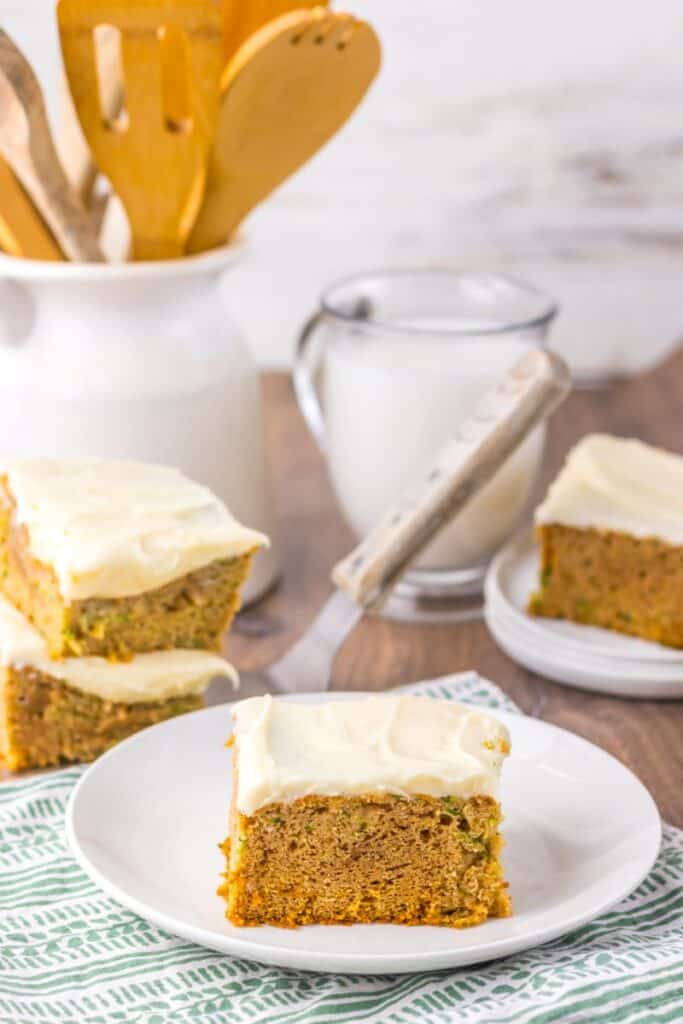 Side view of zucchini cake with white frosting on white plate.