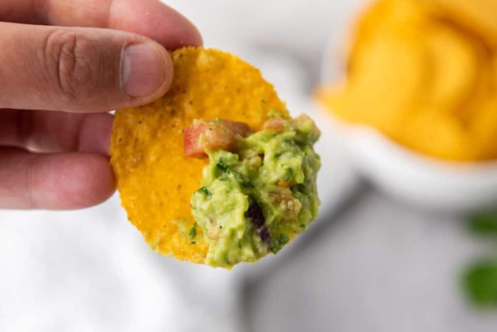 Close up of hand holding tortilla chip dipped in guacamole.