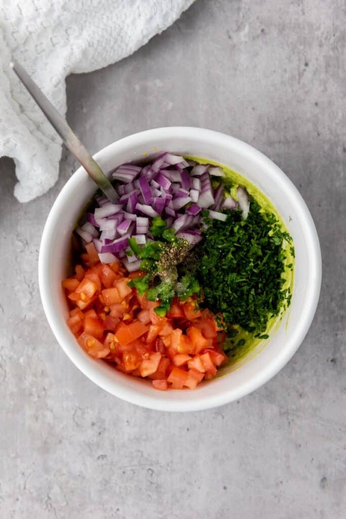 Diced tomatoes, diced red onions, diced jalapenos, and chopped cilantro in white bowl.