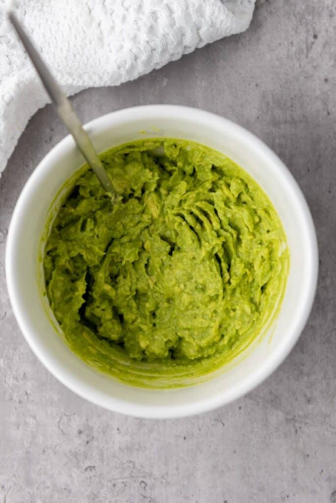Top view of mashed green avocado in white bowl.