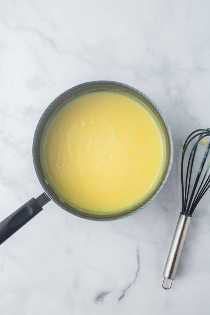 Overhead view of pot of yellow pudding next to whisk.