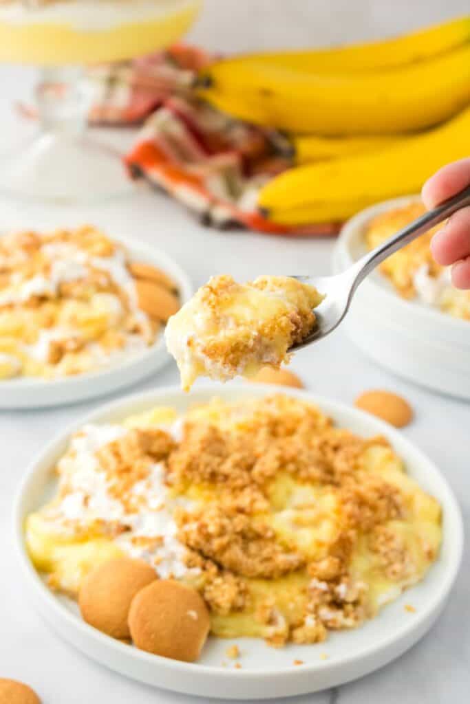 Overhead view of one serving of banana pudding with spoonful held over white plate