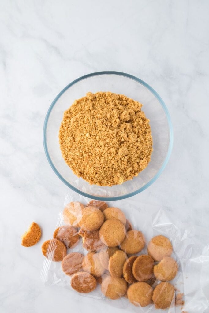 Crushed cookies in glass bowl in front of whole round tan cookies.