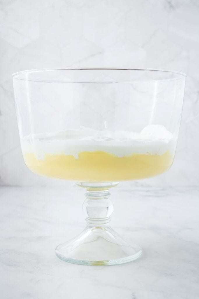 Side view of clear glass trifle bowl with one layer of yellow pudding and one layer of whipped cream.