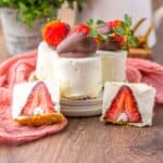 Side view of mini cheesecakes with strawberries inside and a chocolate covered strawberry on top.