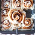 Close up of one glazed cinnamon roll above a square pan of cinnamon rolls.