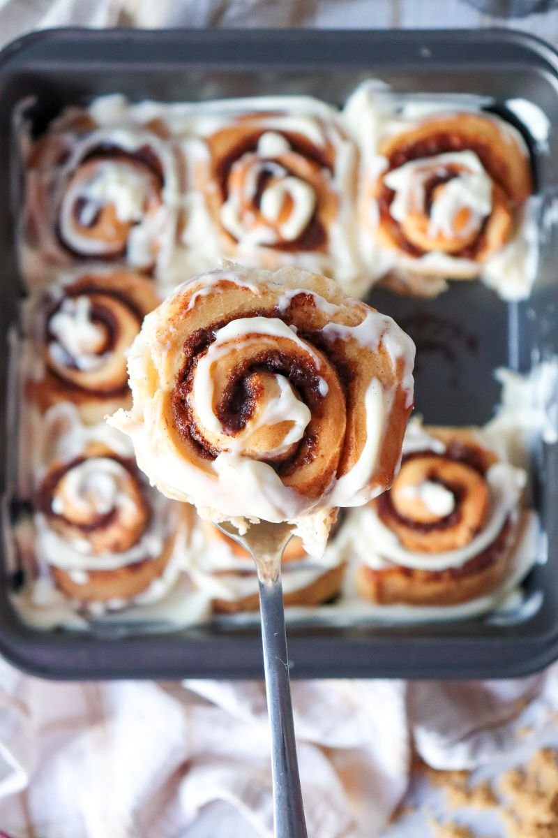 Close up of one glazed cinnamon roll above a square pan of cinnamon rolls.