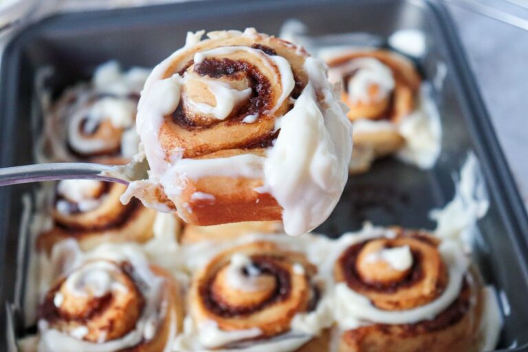 Close up of a glazed cinnamon roll above a pan of cinnamon rolls.
