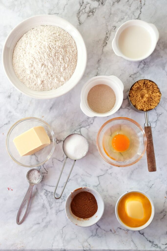 Overhead view of ingredients for cinnamon rolls in white bowls.