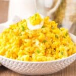 Side view of yellow macaroni salad with half of a deviled egg on top in white bowl.