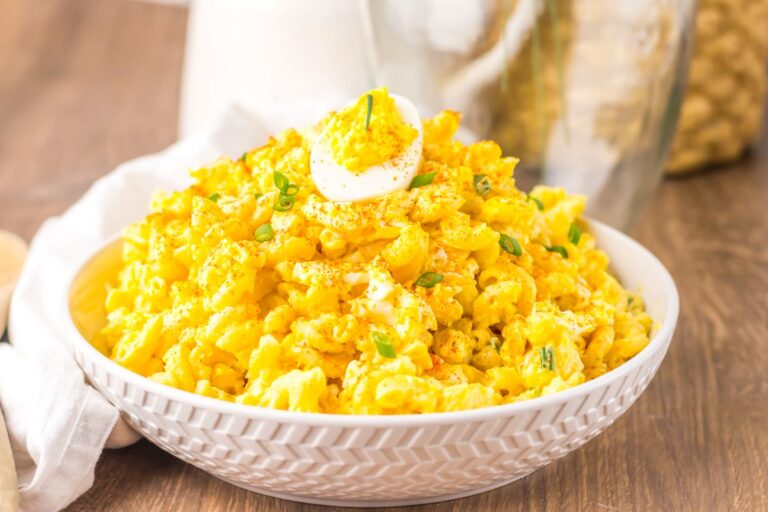 Side view of yellow macaroni salad with half of a deviled egg on top in white bowl.