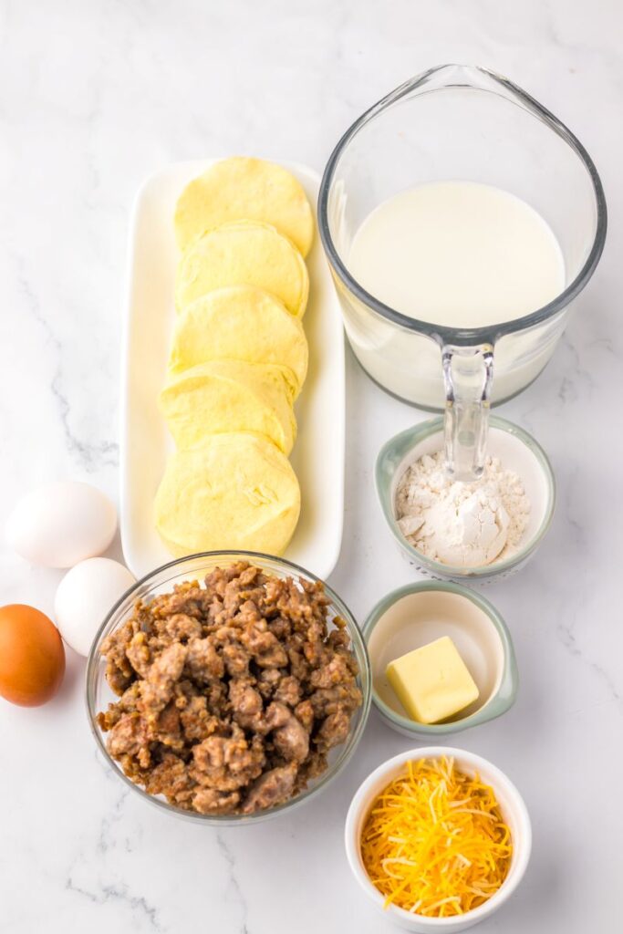 Top view of ingredients for sausage biscuits and gravy casserole in white bowls.