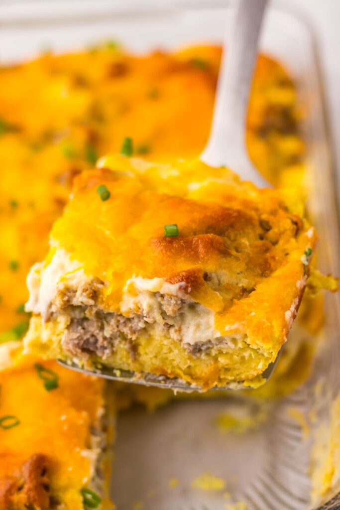 Close up of one serving of breakfast casserole on serving tool above casserole dish.